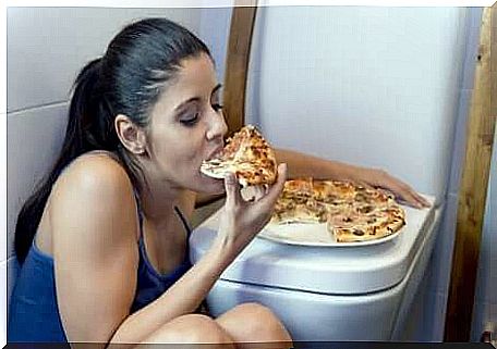 Girl eats pizza leaning on the toilet.